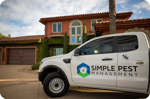 A white Simple Pest service truck parked in the driveway of a large residential home.
